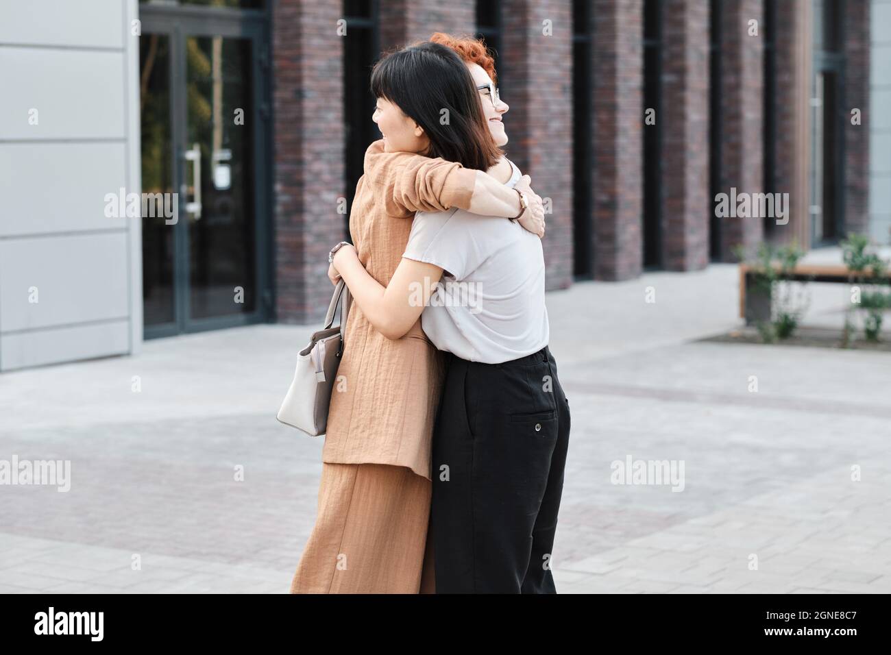 Horizontale mittellange Aufnahme moderner kaukasischer und junger asiatischer Frauen, die sich im Freien umarmen Stockfoto
