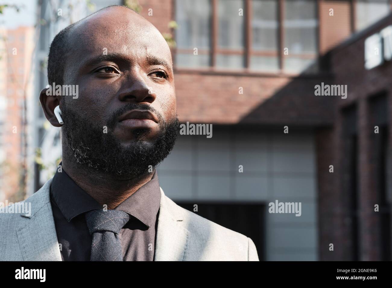 Horizontales Nahaufnahme-Porträt eines selbstbewussten, reifen afroamerikanischen Mannes mit Bart im Gesicht und Ohrstöpseln, der im Freien unterwegs ist und Musik hört, die wie ein aussieht Stockfoto