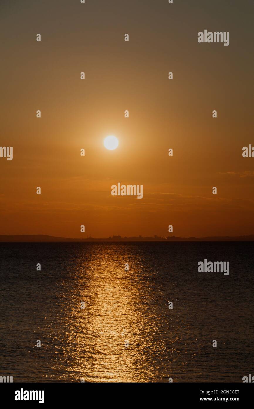 Streifen von Sonnenlicht über den Kanal mit einem rötlichen Glanz am Horizont Stockfoto