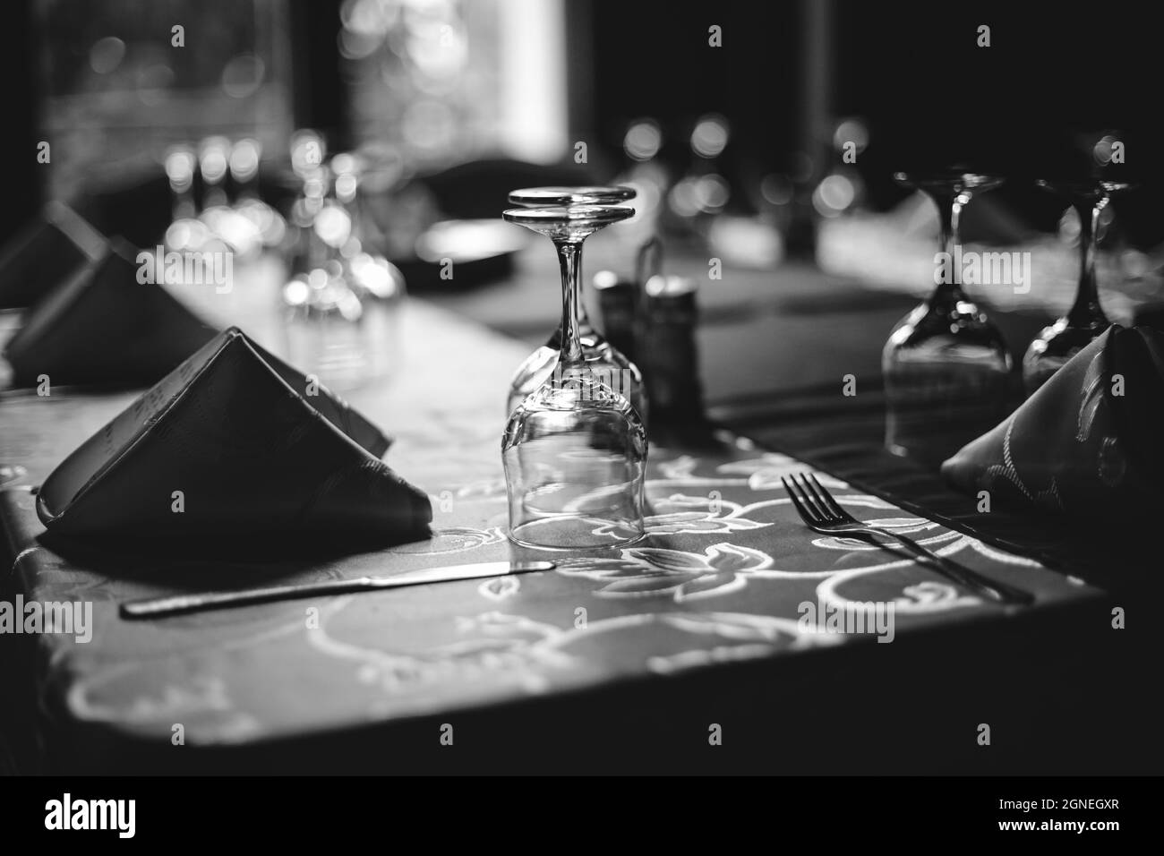 Bild mit geringer Schärfentiefe (selektiver Fokus) und einem Restauranttisch, der bereit ist, Kunden zu empfangen. Leere Gläser und Geschirr. Stockfoto