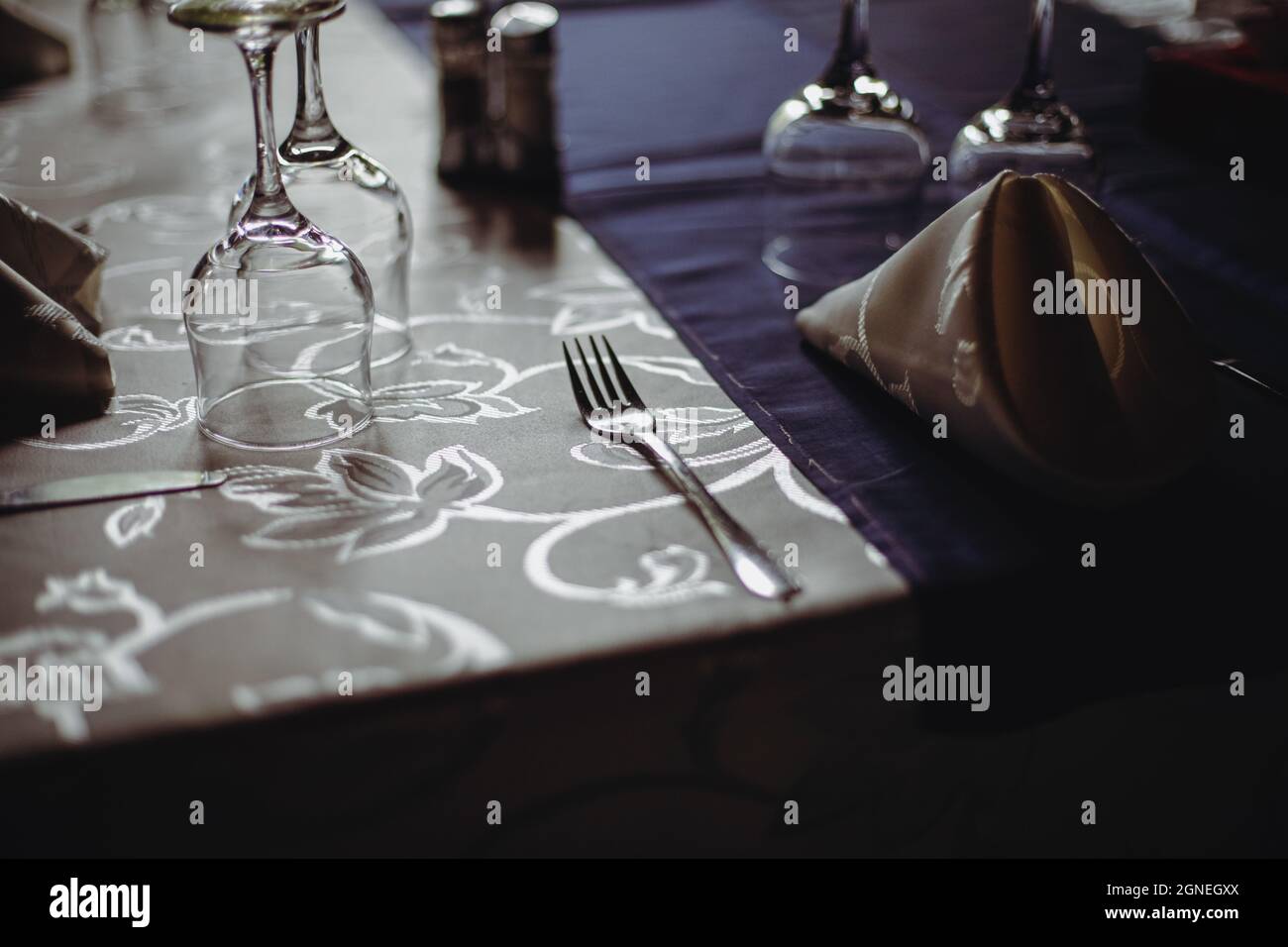 Bild mit geringer Schärfentiefe (selektiver Fokus) und einem Restauranttisch, der bereit ist, Kunden zu empfangen. Leere Gläser und Geschirr. Stockfoto