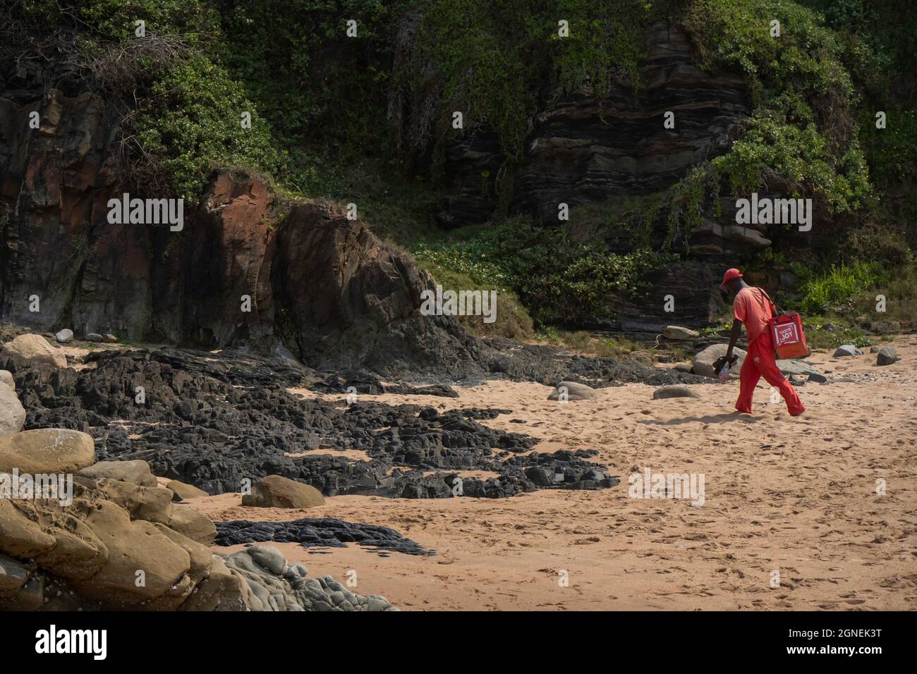 Durban, Südafrika - 21. September 2019: Eis Verkäufer in rot Spaziergänge am Strand mit seinem Kühlerkasten auf der Suche nach Kunden. Stockfoto