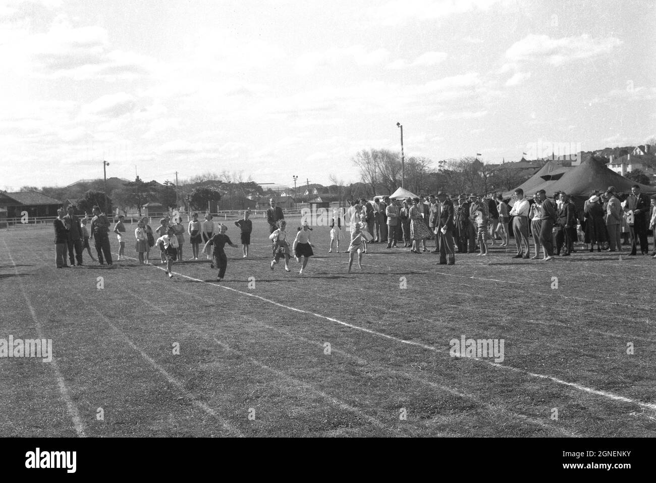 Historische 1950er Jahre, Eltern und Lehrer beobachten, wie kleine Kinder an einem Laufrennen teilnehmen, dem 100-Meter-Rennen, draußen auf einem Grasfeld an einem Grundschule-Sporttag, England, Großbritannien. Stockfoto