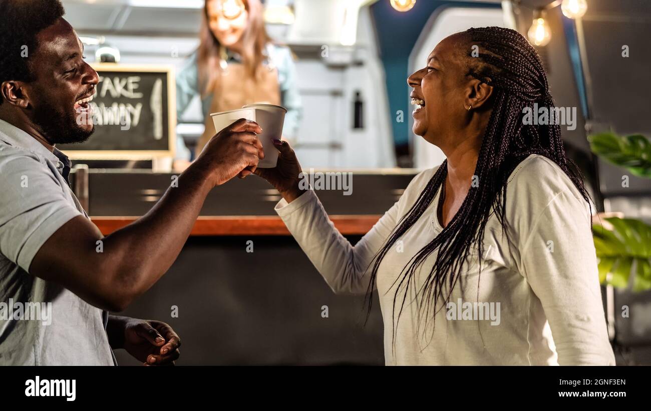 Glückliche afrikanische Familie, die Spaß beim Toasten mit Bier auf einem Straßenmarkt für Lebensmittel-Lastwagen im Freien hat Stockfoto