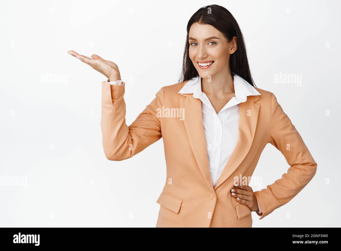 Erfolgreiche Geschäftsfrau, die das Produkt vorführt, auf leeren Raum zeigt, Werbung zeigt und lächelt und auf weißem Hintergrund in Anzug steht Stockfoto