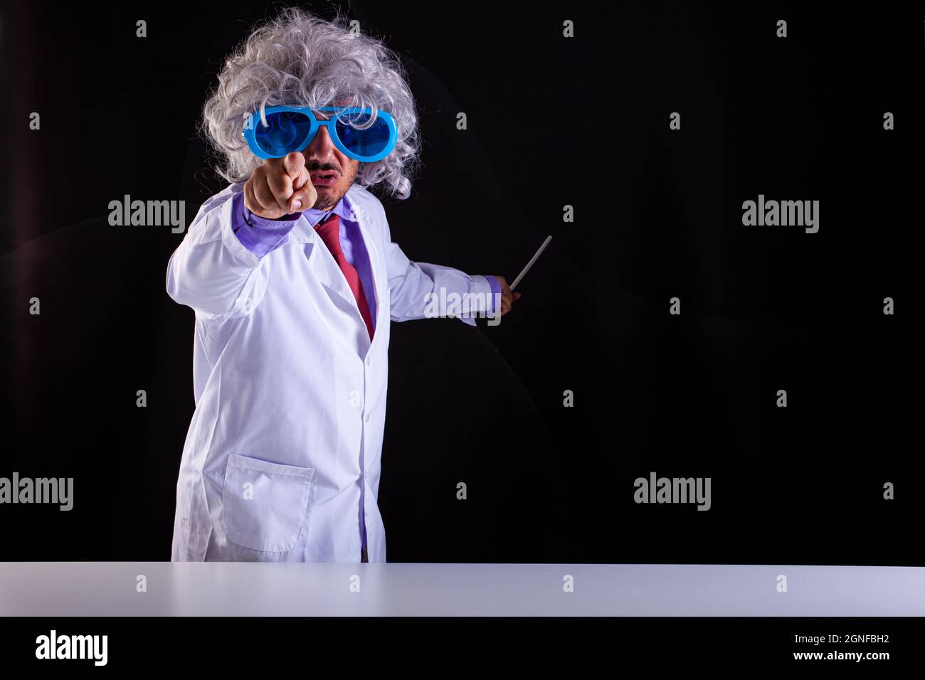 Wütender Wissenschaftslehrer im weißen Mantel mit ungepflegten Haaren in lustigen Augenbrillen zeigt mit seinem Finger auf schwarzen Hintergrund Stockfoto