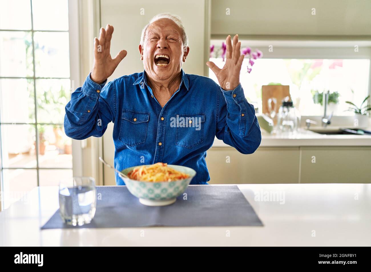 Älterer Mann mit grauen Haaren, der zu Hause Pasta-Spaghetti isst, ist ...