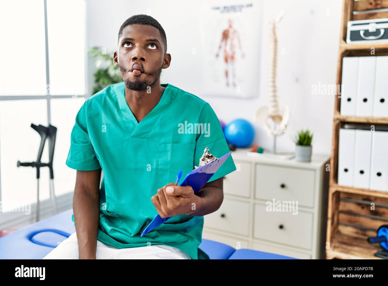 Junger afroamerikanischer Mann, der in der Schmerzklinik arbeitet, macht Fische mit Lippen, verrückte und komische Geste. Lustiger Ausdruck. Stockfoto