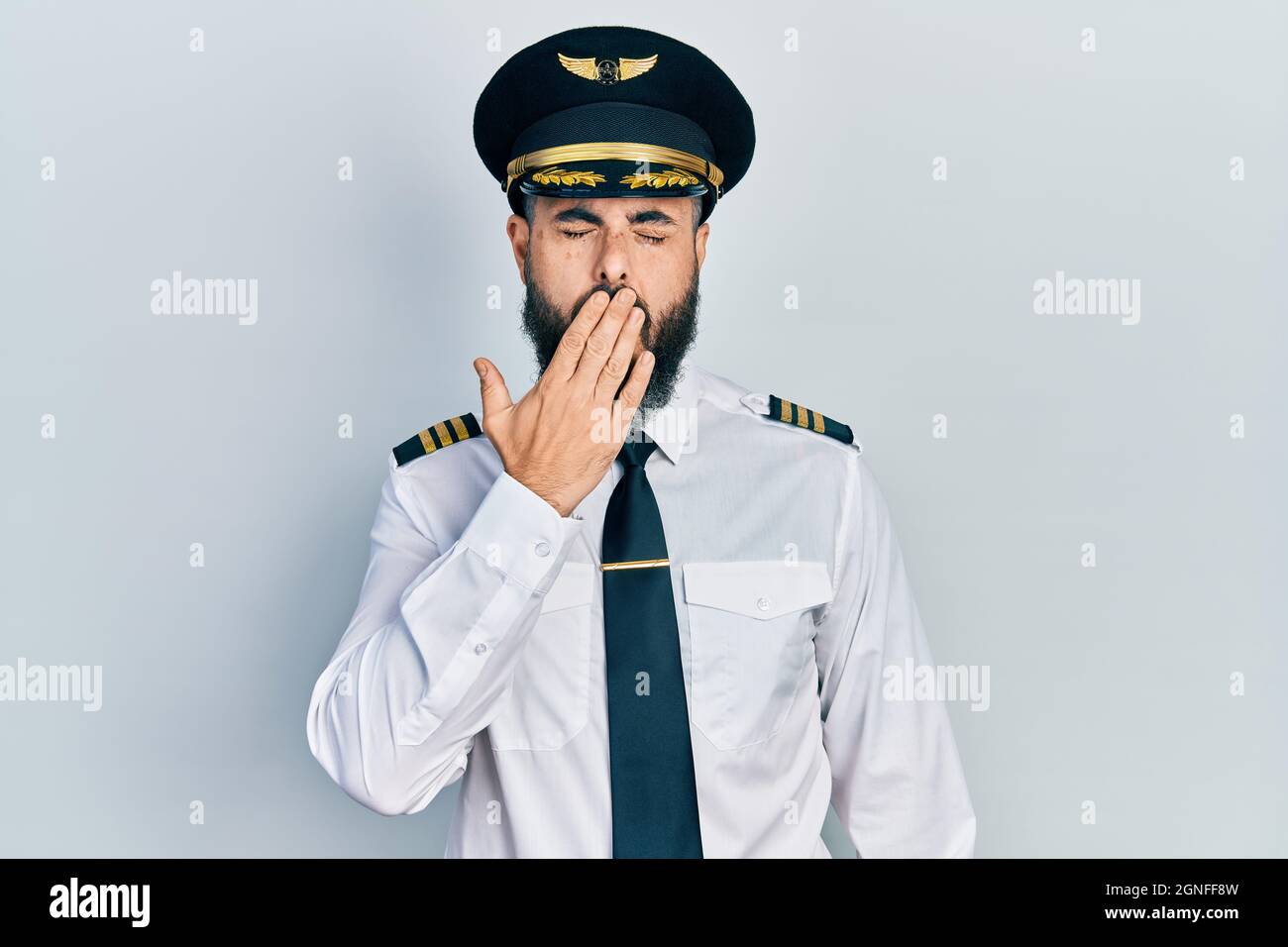 Junge hispanic Mann trägt Flugzeug Pilot Uniform gelangweilt Gähnen müde Abdeckung Mund mit der Hand. Unruhig und Schläfrigkeit. Stockfoto