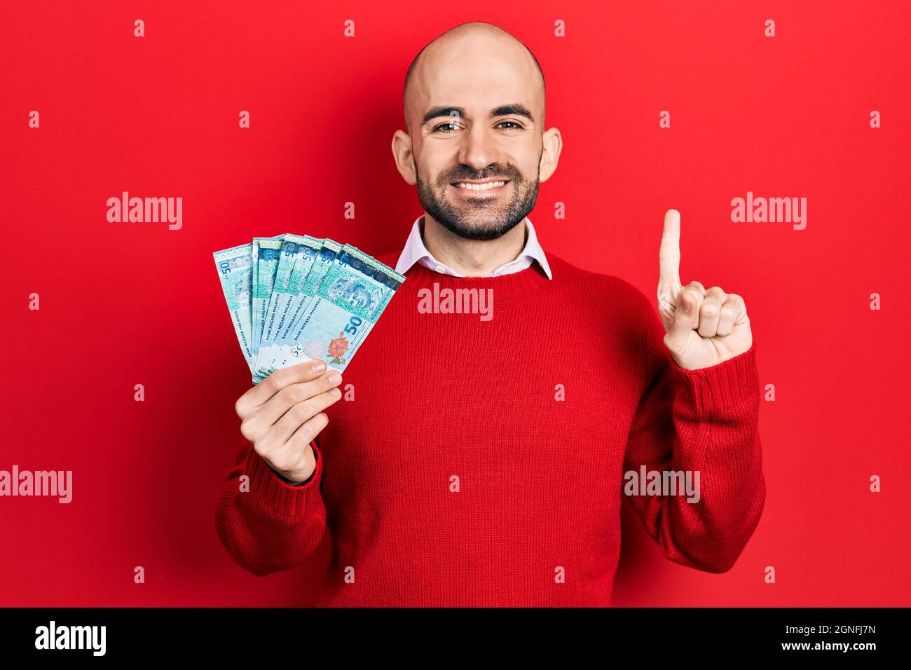 Junger kahler Mann mit 50 malaysischen Ringgit-Banknoten, lächelnd mit einer Idee oder Frage, die mit dem Finger mit einem glücklichen Gesicht zeigt, Nummer eins Stockfoto