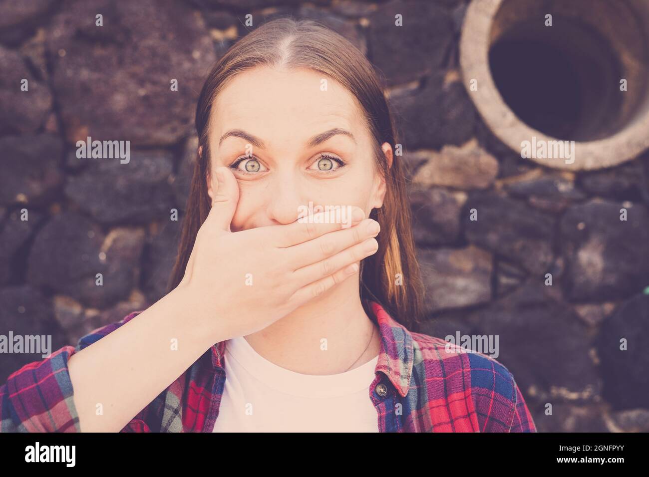 Nahaufnahme einer schockierten Frau, die den Mund mit der Hand bedeckt, die gegen eine Steinmauer steht. Porträt einer schönen Frau mit durchbohrter Nase. Frau, die ihren Mout bedeckt Stockfoto