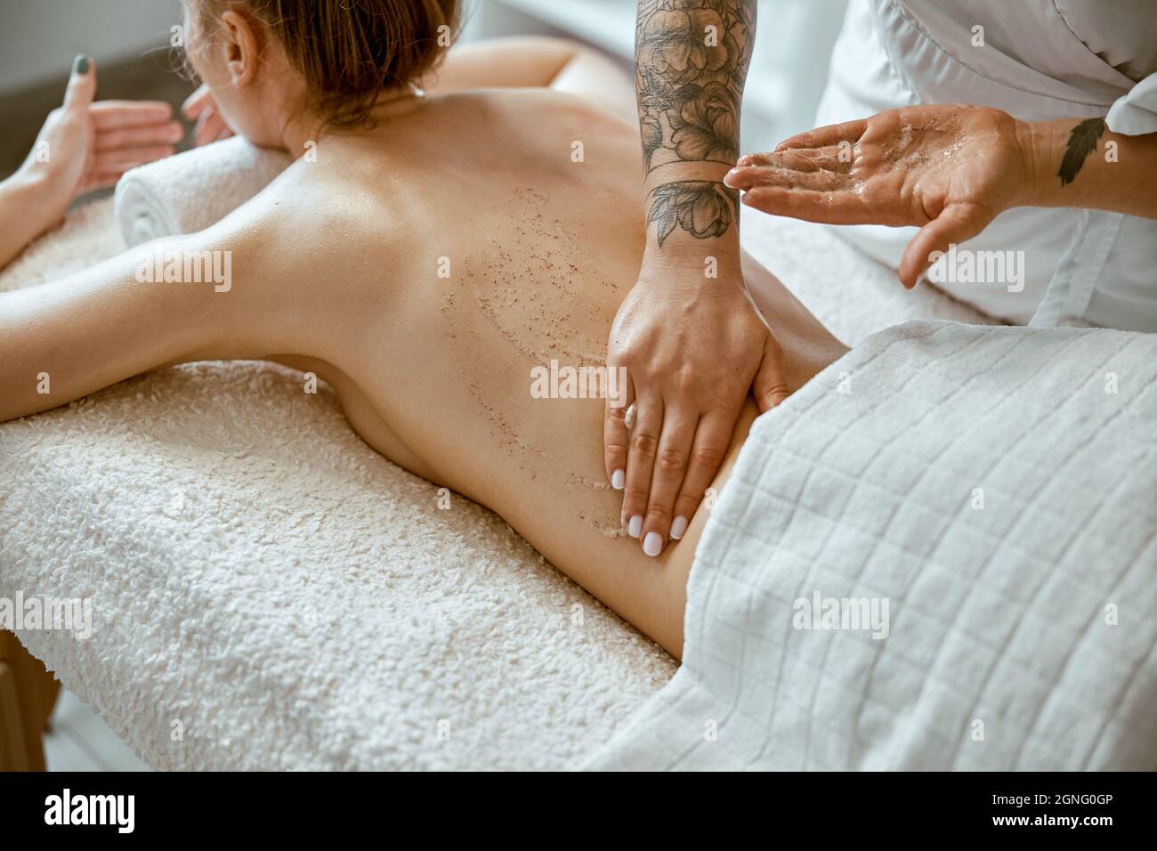 Selbstbewusste weibliche Spezialistin tut entspannende Körpermassage für schöne schlanke kaukasische Dame im minimalistischen Spa-Salon Stockfoto