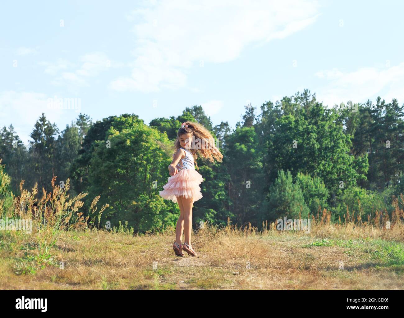 Schönes kleines Mädchen, das im sonnigen Frühlingspark mit Blumen tanzt. Happy niedlichen Kind Spaß im Freien bei Sonnenuntergang. Stockfoto