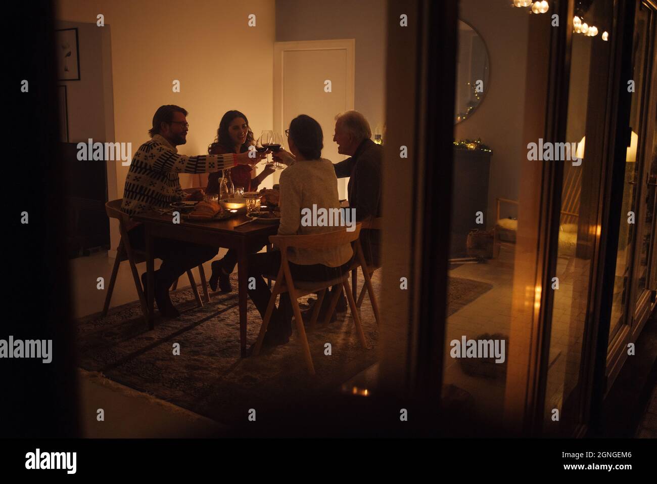 Familie, die am Heiligabend am Esstisch Wein toasting. Familie, die ein gemeinsames Weihnachtsessen in einem gemütlichen skandinavischen Zuhause hat. Stockfoto