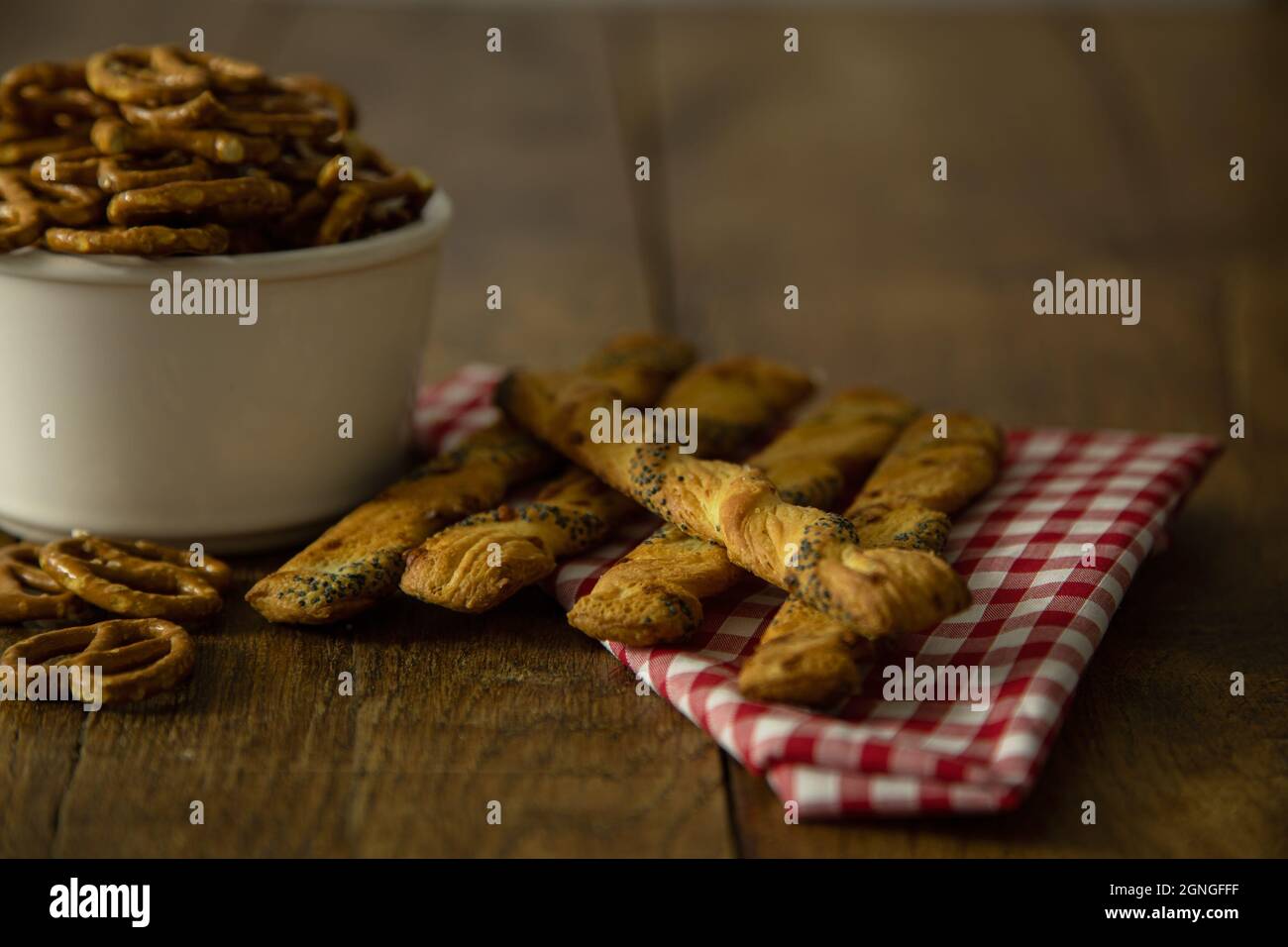 Brotstangen und Schüssel mit gesalzenen Brezelsnacks mit roter Karo-Serviette auf altem Eichentisch Stockfoto