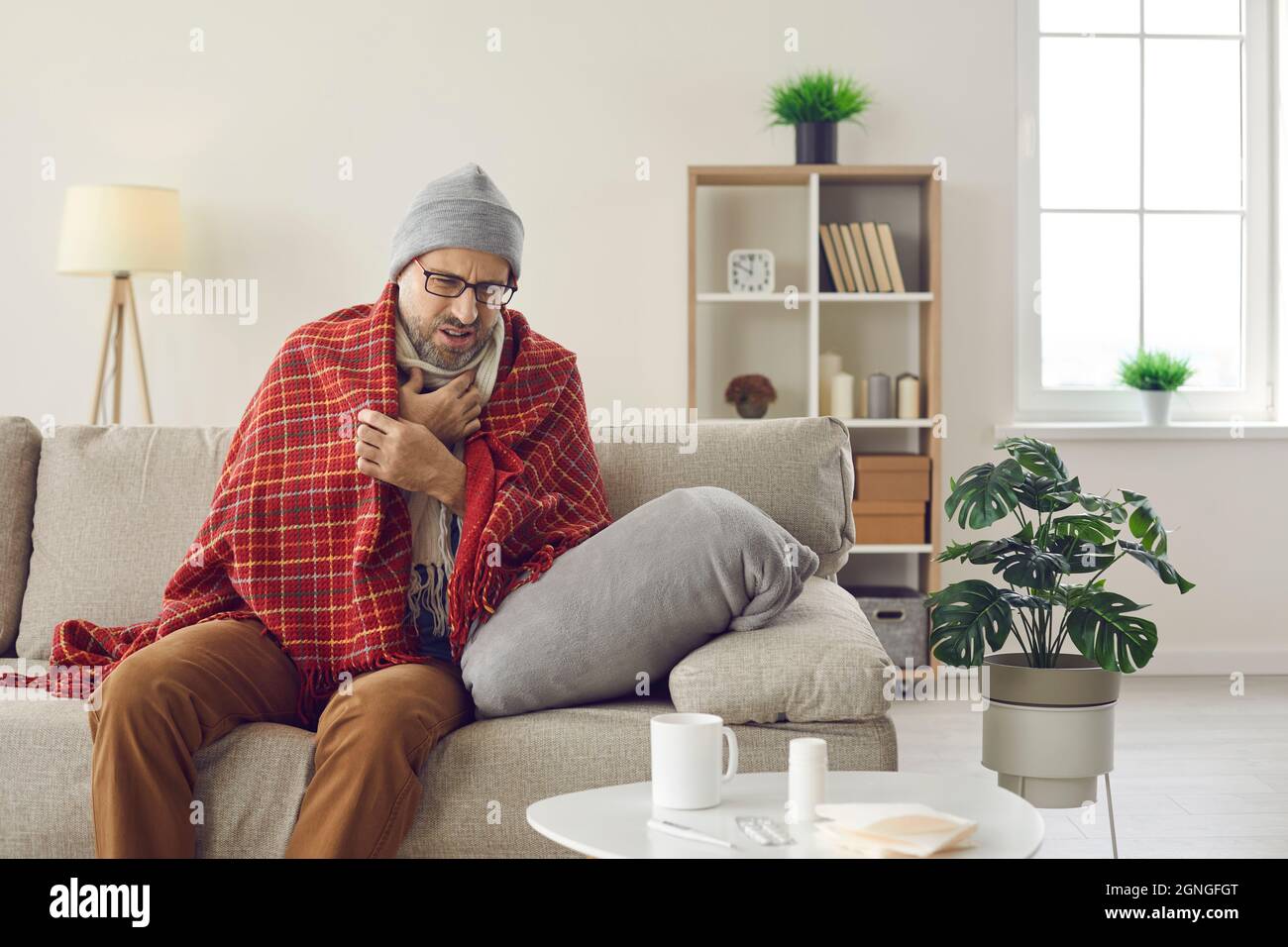 Mann mittleren Alters, der Erkältung oder Grippe hat, sitzt zu Hause auf der Couch und hustet Stockfoto