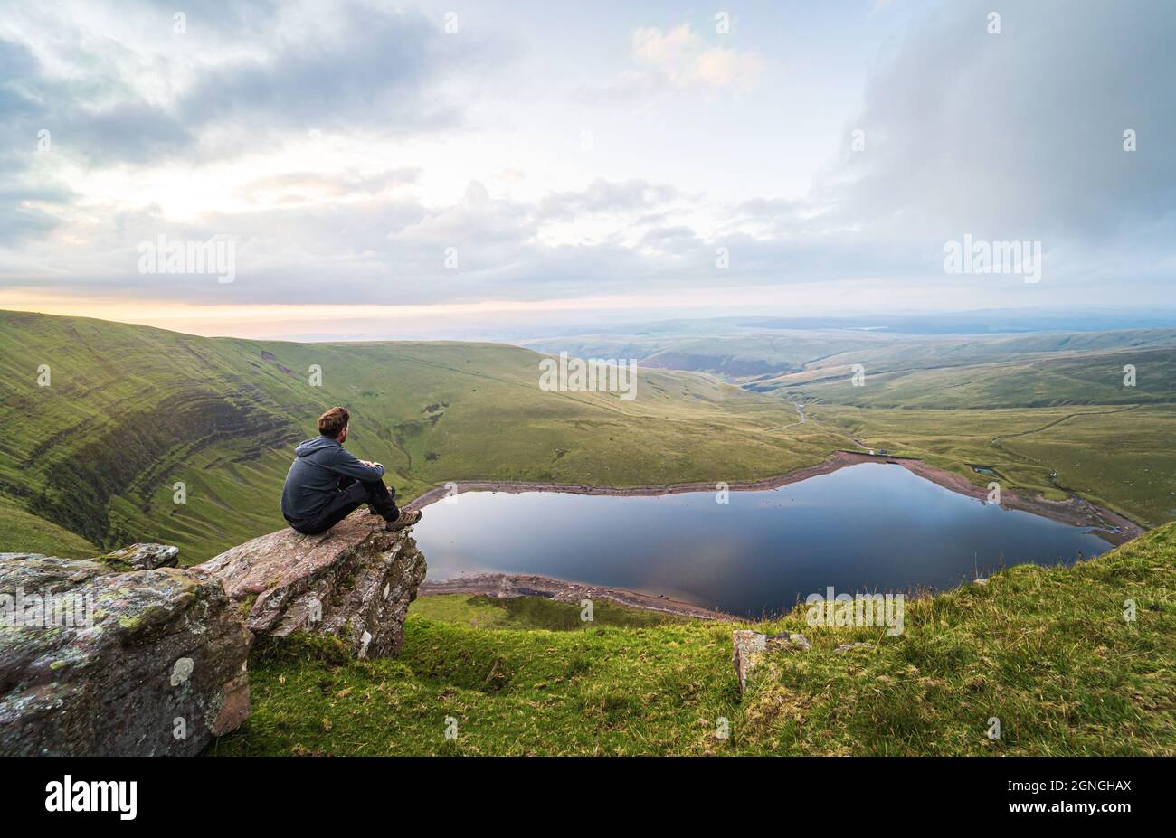 Der Mann sitzt auf einem Felsen und blickt auf den See Llyn y Fan Fach. Brecon Beacons National Park. Black Mountain, Carmarthenshire, South Wales, Vereinigtes Königreich. Stockfoto