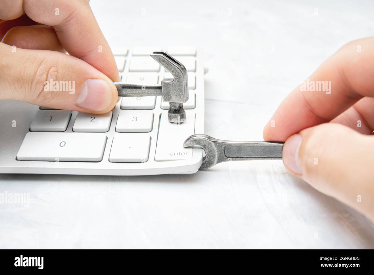 Reparieren einer festgeklemmten Taste auf einer weißen Tastatur mit kleinem Hammer und Schraubenschlüssel. Kreatives Konzept der Verwendung nicht autorisierter Reparaturwerkstätten. Stockfoto