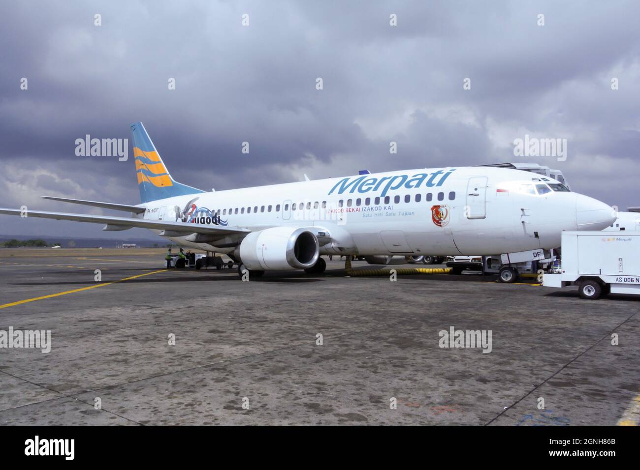 Flugzeug von Merpati Airlines vorbereitet für den Flug auf dem Vorfeld des I Gusti Ngurah Rai International Airport mit dramatischen und dunklen bewölkten Himmel. Keine Personen. Stockfoto