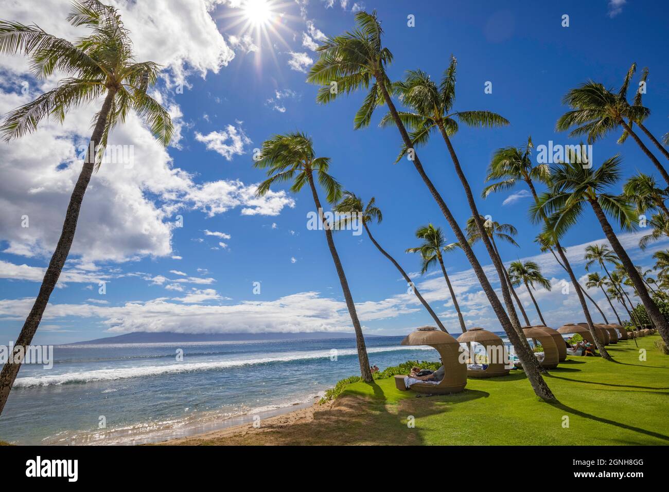 Palmen und Cabanas Reihen sich entlang des weltberühmten Ka'anapali Beach mit der Insel Lanai gegenüber dem Kanal, Maui, Hawaii. Stockfoto