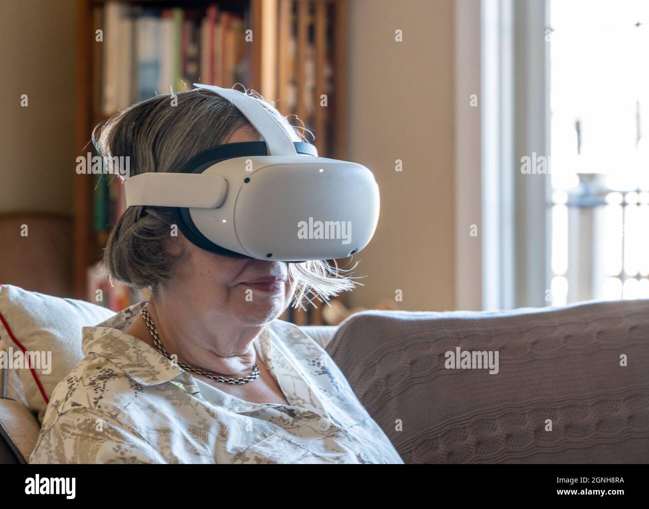 Eine ältere Dame saß zu Hause und schaute sich einen Film oder eine Quest-App auf einem modernen Virtual Reality VR-Headset an Stockfoto