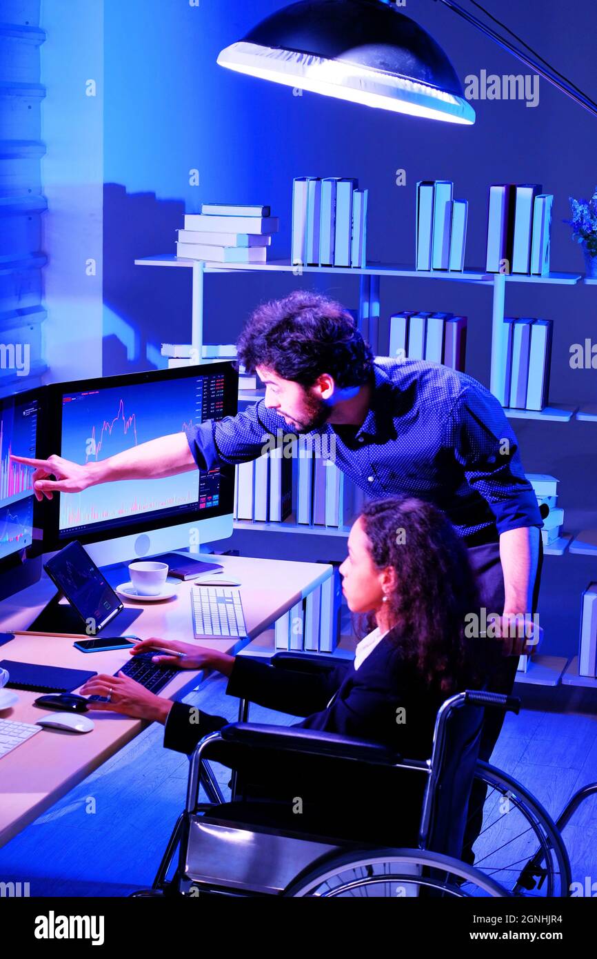 Ein Mann zeigt einer Frau während der nächtlichen Überstunden in einem Büro den obersten Punkt der Balkengrafik auf dem Computerbildschirm Stockfoto