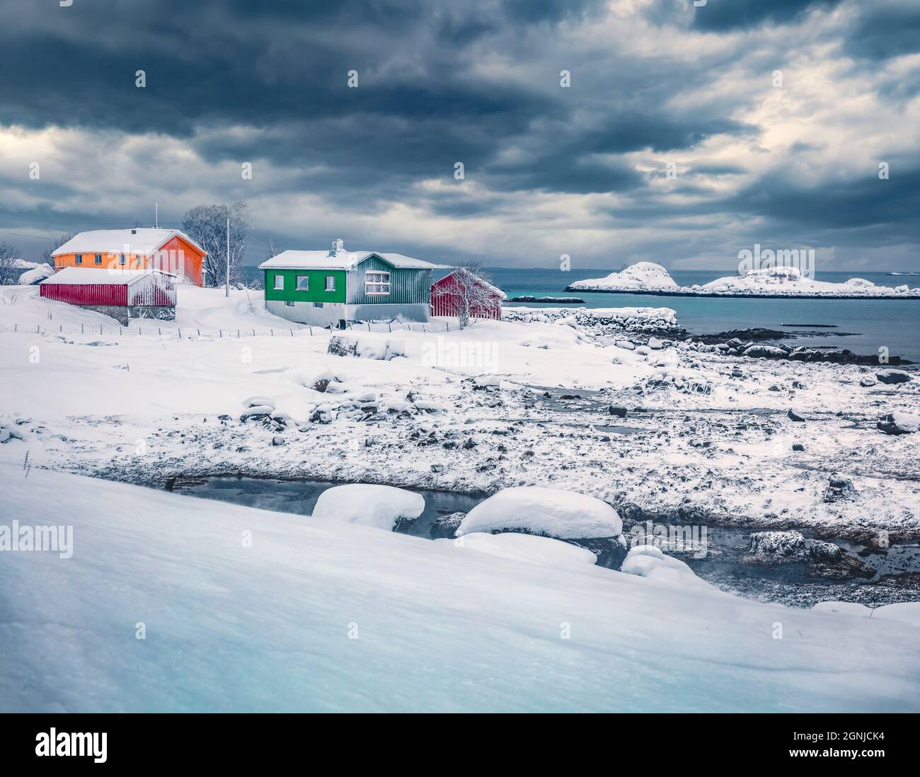Dramatische Winterszene des Fischerdorfes Justad auf der Insel Vestvavoy. Bunte Holzhäuser auf den Lofoten-Inseln, traditionelle norwegische Architektur. Tr Stockfoto
