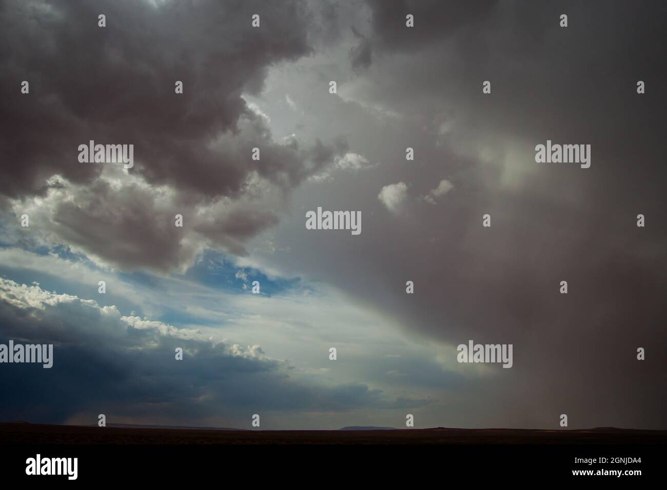 Dramatische Landschaft mit herannahenden Wetterfronten mit dunkelgrauen und weißen Wolken und blauem Himmel mit Sonnenstrahlen über dem schlichten Horizont Stockfoto