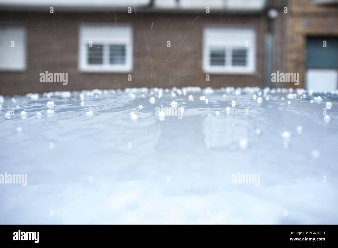 Hagel fällt über das Autodach. Selektiver Fokus auf den städtischen Hintergrund Stockfoto