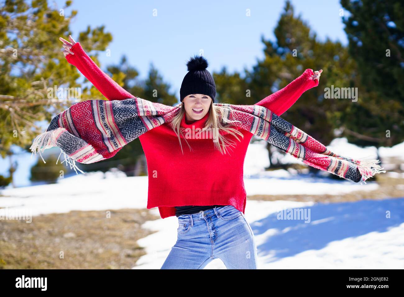 Junge glückliche junge blonde Frau winkt ihren Schal im Wind in einem Wald in den verschneiten Bergen. Stockfoto