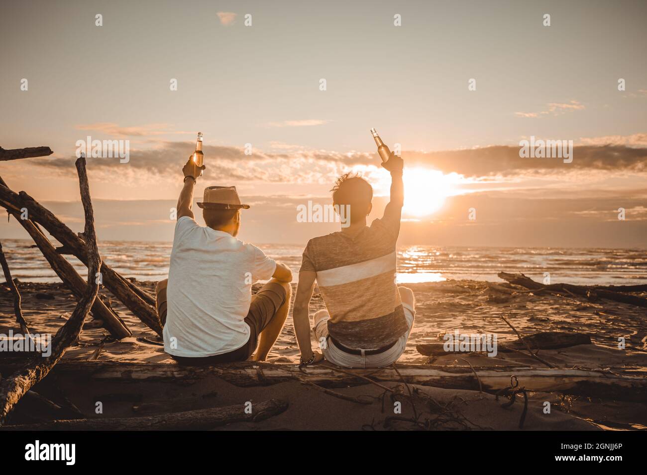 Zwei junge Freunde verbringen Zeit zusammen am Strand, trinken Bier und toasten im Urlaub in der Dämmerung Sommer Sonnenuntergang. Freundschaftskonzept Stockfoto