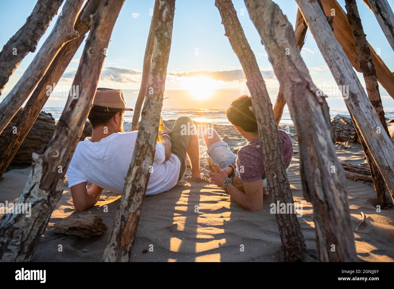 Zwei junge Freunde verbringen Zeit zusammen am Strand, trinken Bier und toasten im Urlaub in der Dämmerung Sommer Sonnenuntergang. Freundschaftskonzept Stockfoto