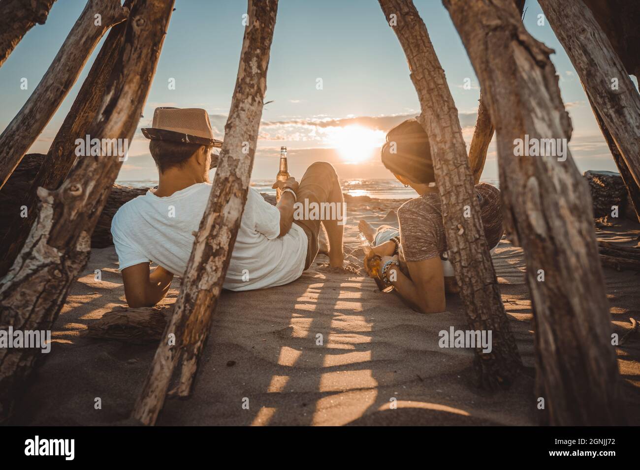 Zwei junge Freunde verbringen Zeit zusammen am Strand, trinken Bier und toasten im Urlaub in der Dämmerung Sommer Sonnenuntergang. Freundschaftskonzept Stockfoto