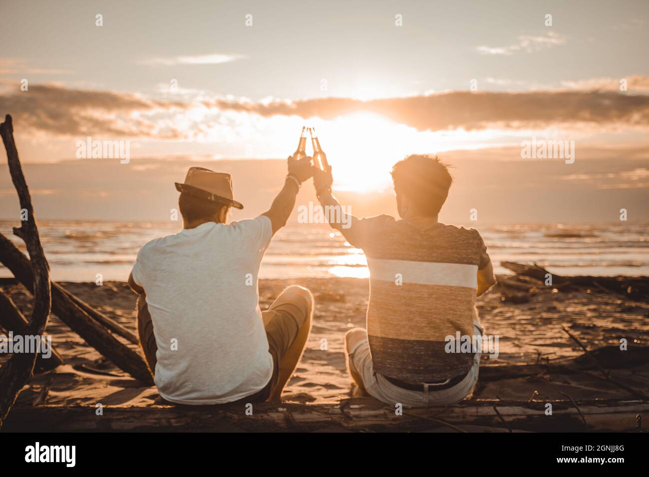 Zwei junge Freunde verbringen Zeit zusammen am Strand, trinken Bier und toasten im Urlaub in der Dämmerung Sommer Sonnenuntergang. Freundschaftskonzept Stockfoto