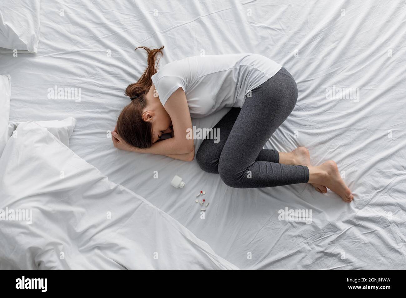 Traurige Verzweiflung junge kaukasische Frau, die unter Bauchschmerzen leidet, die mit einem Glas und verstreuten Pillen auf dem Bett lagen Stockfoto