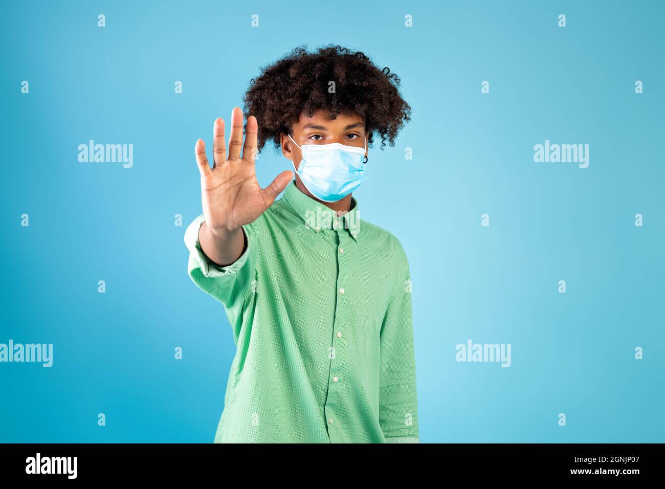 Teen schwarz Kerl im Gesicht Maske gestikulieren STOPPEN, zum Ausdruck Negativität gegenüber Coronavirus Pandemicon, blauer Hintergrund, Stockfoto