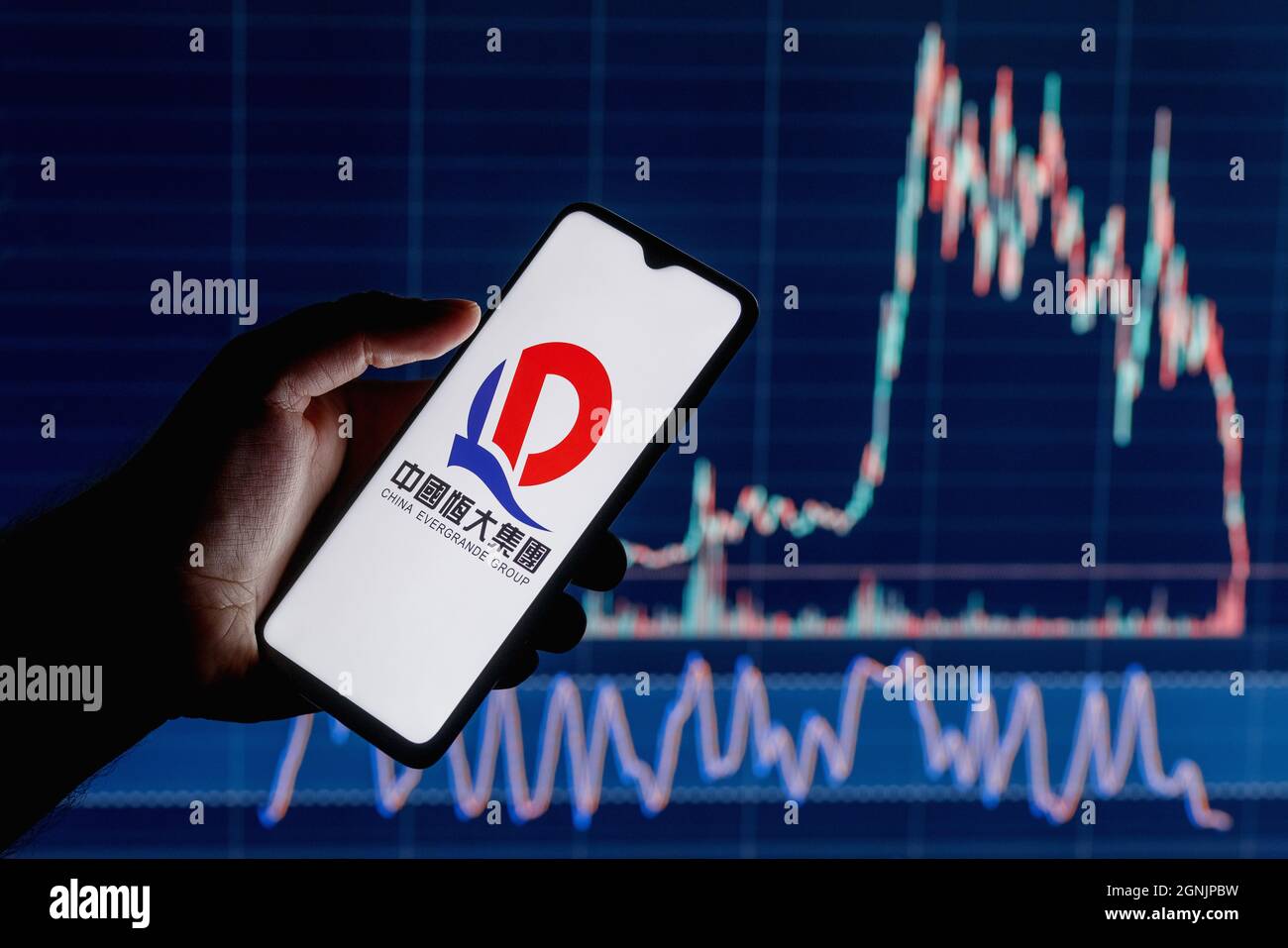 Ein Smartphone mit dem Evergrande-Logo in der Hand. Aktiendiagramm im Hintergrund. Stockfoto