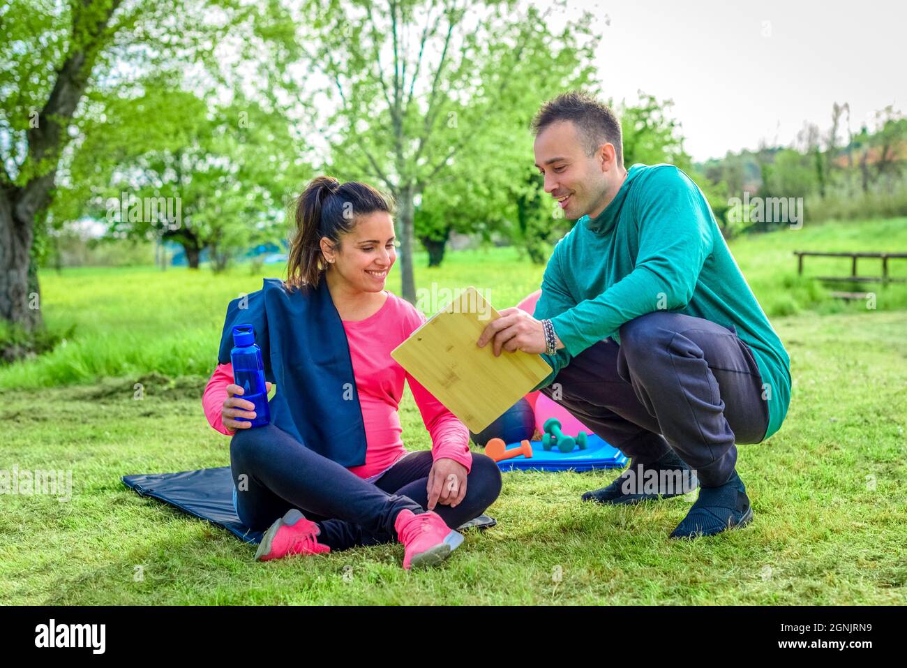 Ein Paar von Personal Trainer und eine junge Studentin Frau schwanger diskutieren Trainingsplan zusammen lächelnd im Freien. Fitness und gesunde Lebensweise Stockfoto