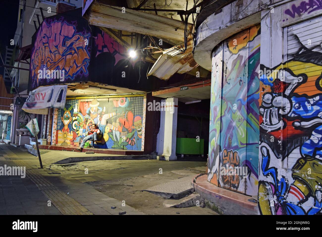 Nächtliche Straßenszene in Surakarta auf Java: Der Mann vor einer bunten Grafitti sieht auf seinem Smartphone gelangweilt aus Stockfoto