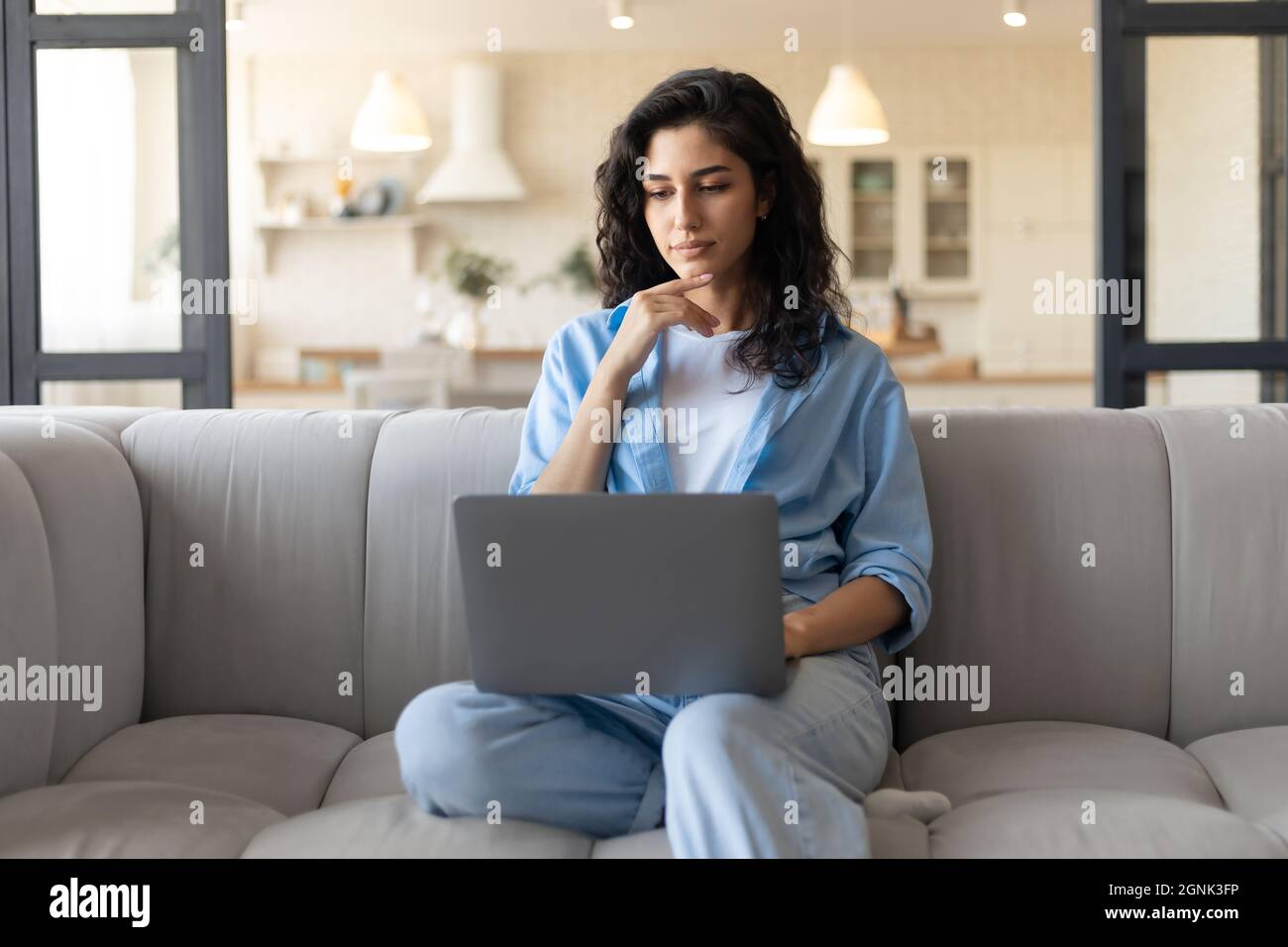 Seriöse junge Frau, die mit einem Laptop auf der Couch sitzt, von zu Hause aus arbeitet oder studiert Stockfoto