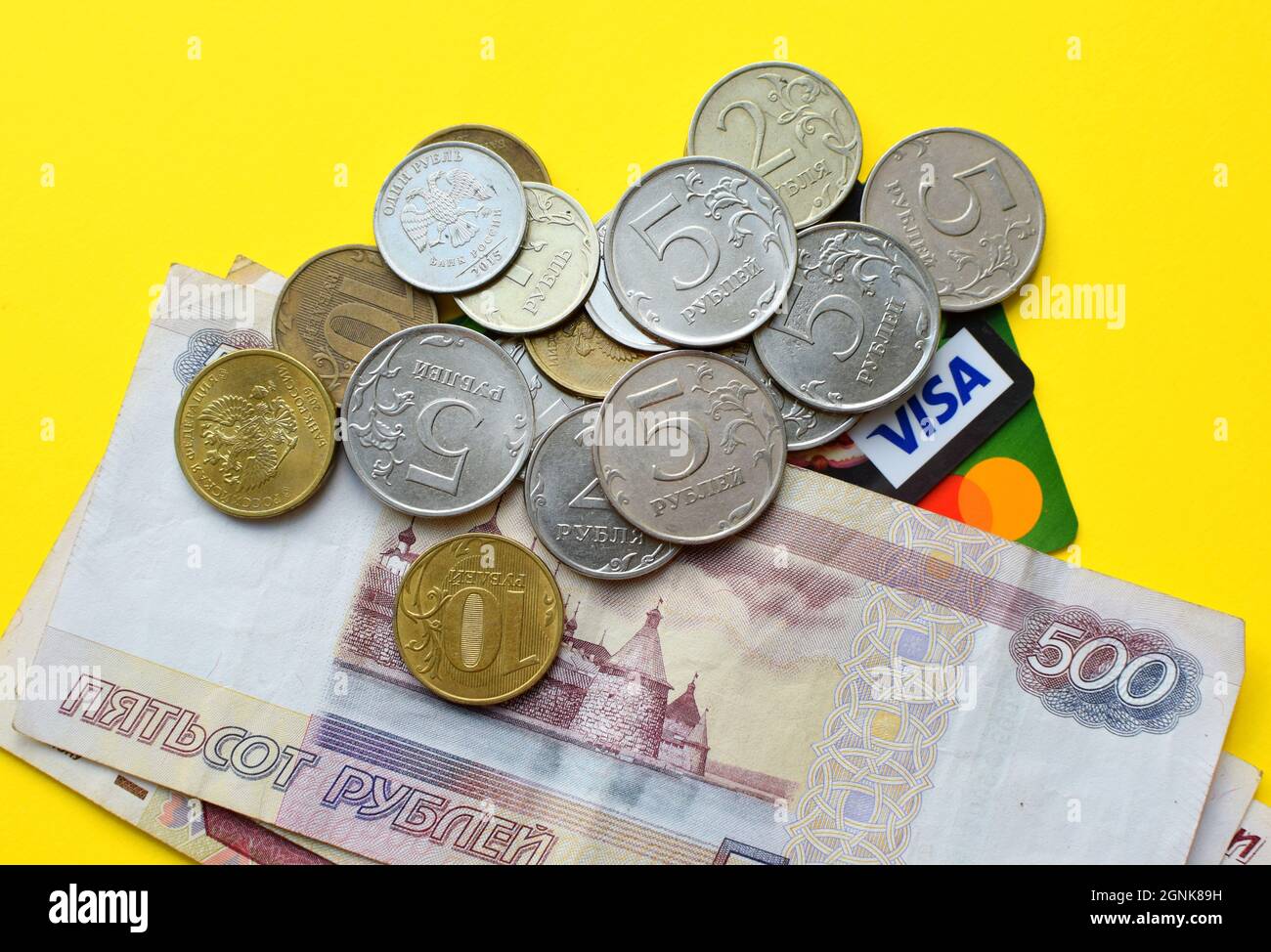 Russische Rubel auf gelbem Hintergrund. Banknoten, verschiedene Münzen und Kreditkarten Stockfoto