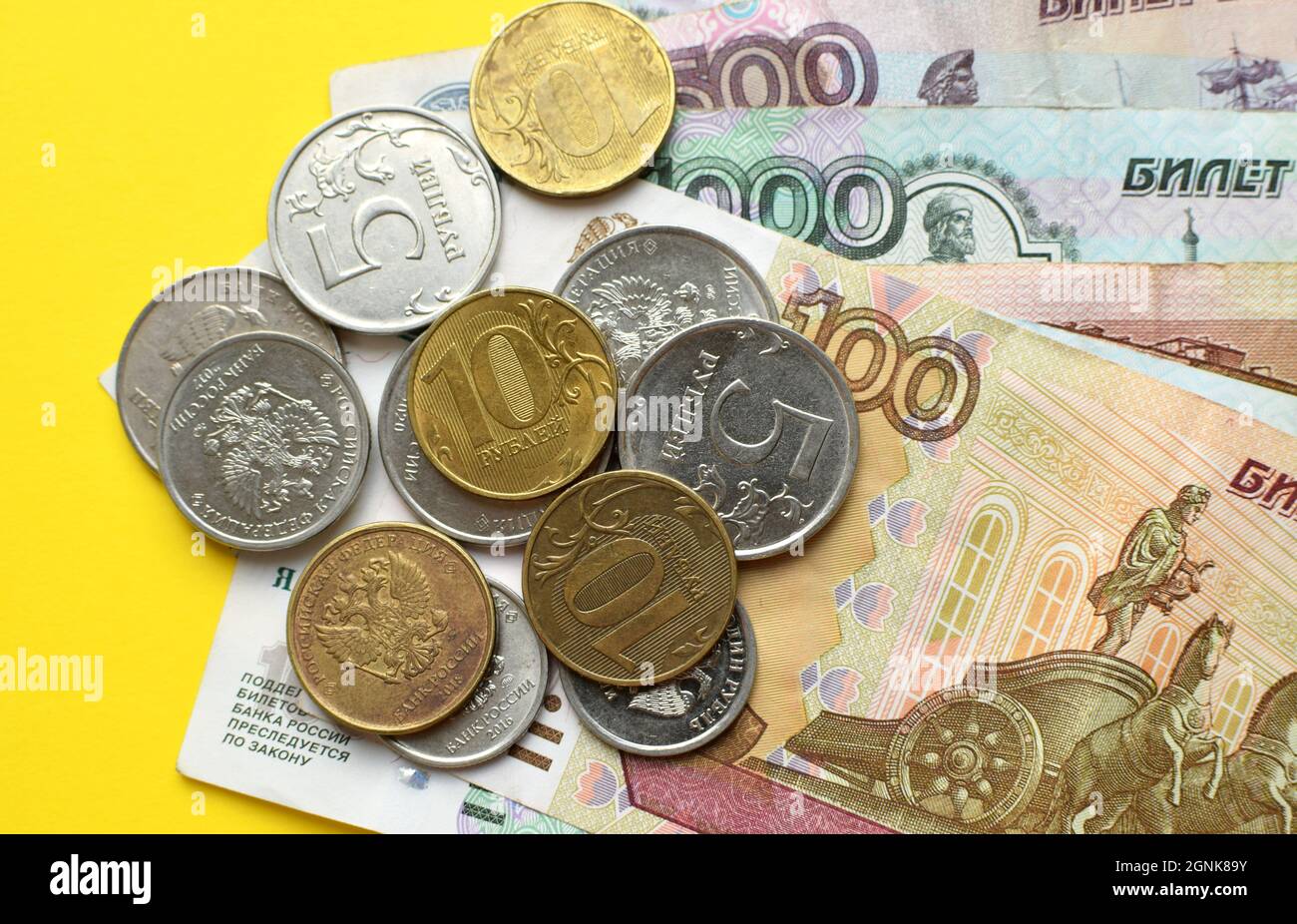 Russische Rubel auf gelbem Hintergrund. Banknoten und verschiedene Münzen. Stockfoto