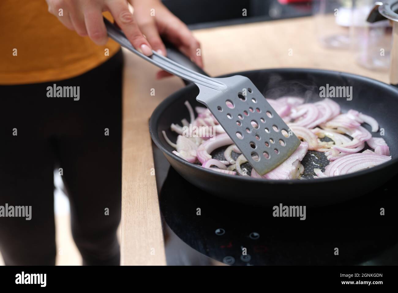 Frau frittiert Zwiebeln in Pfanne in der Küche Nahaufnahme Stockfoto