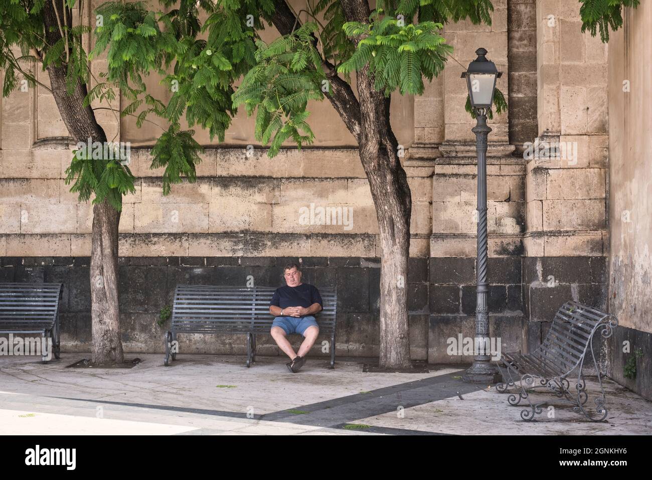 Ein Mann, der an einem heißen Sommernachmittag vor der barocken Kathedrale von Acireale aus dem 17. Jahrhundert auf der Piazza Duomo in Acireale im Schatten schläft. Catania, Sizilien, Italien Stockfoto