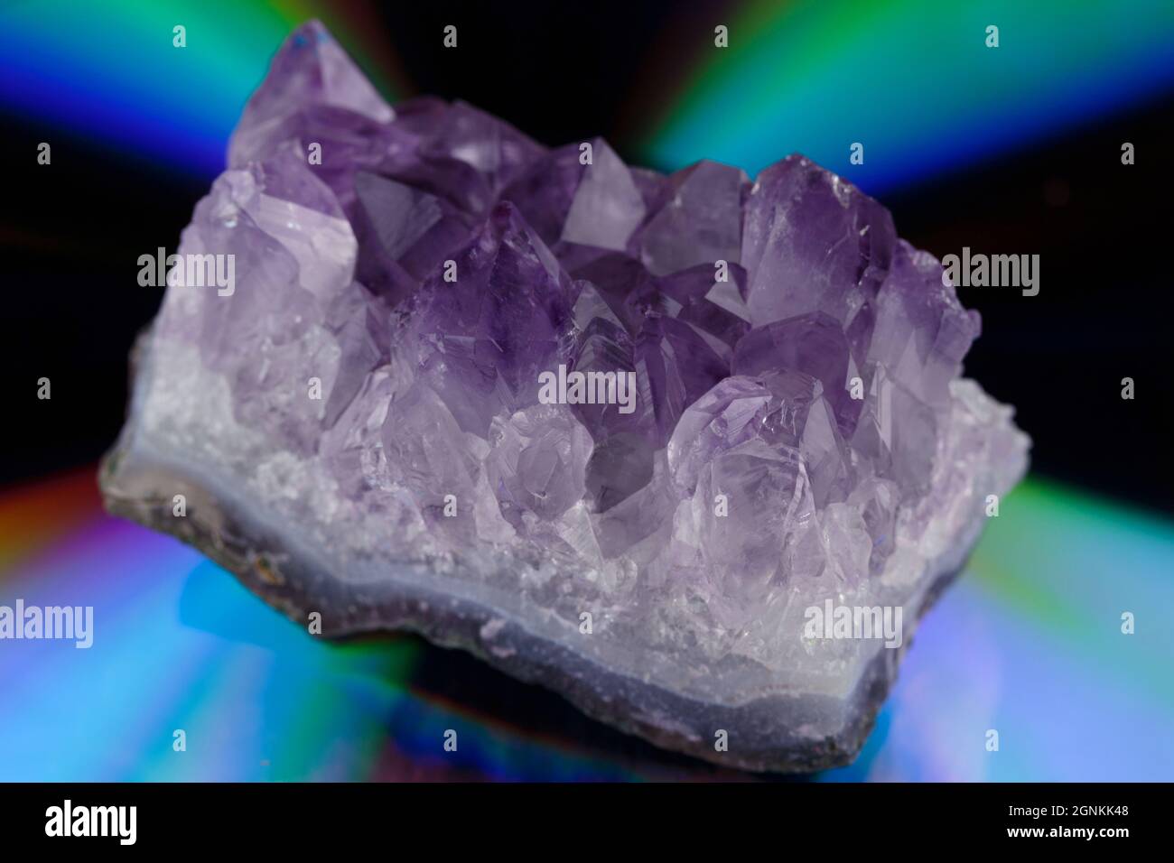 Ein purpurroter, roher Amethyst-Bergkristall auf einem psychedelisch irisierenden, farbenfrohen Hintergrund mit geringer Schärfentiefe Stockfoto