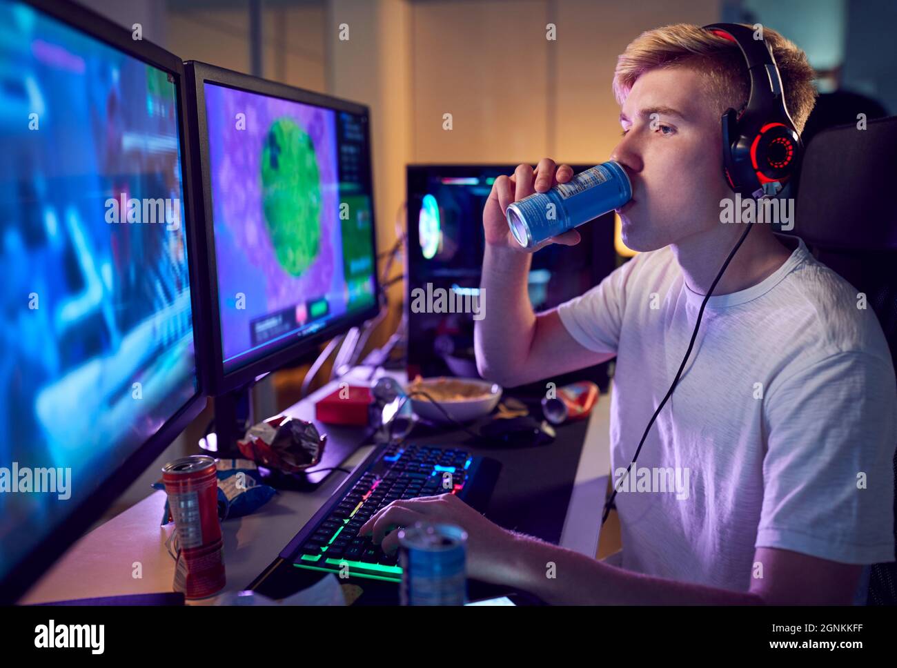 Teenager trinken Koffein Energy Drink spielen zu Hause mit zwei Bildschirmen in der Nacht Stockfoto