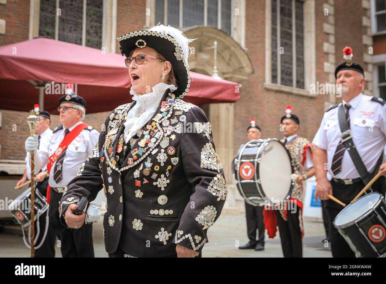 St Mary-Le-Bow, London, Großbritannien. 26. Sep, 2021. A Pearly Queen singt spielerisch mit zu 'IT's A Long Way to Tipperary', während die Band im Hof spielt. Perlkönige und Königinnen feiern ihr jährliches Erntefest mit dem Costermonger´s Harvest Service in der St. Mary-Le-Bow Kirche. Da die üblichen Feierlichkeiten im Guildhall Yard abgesagt werden mussten, treffen sich die Pearlies vor und nach dem Gottesdienst vor seinem Jahr und begrüßen Freunde und die Öffentlichkeit vor der Kirche. Kredit: Imageplotter/Alamy Live Nachrichten Stockfoto