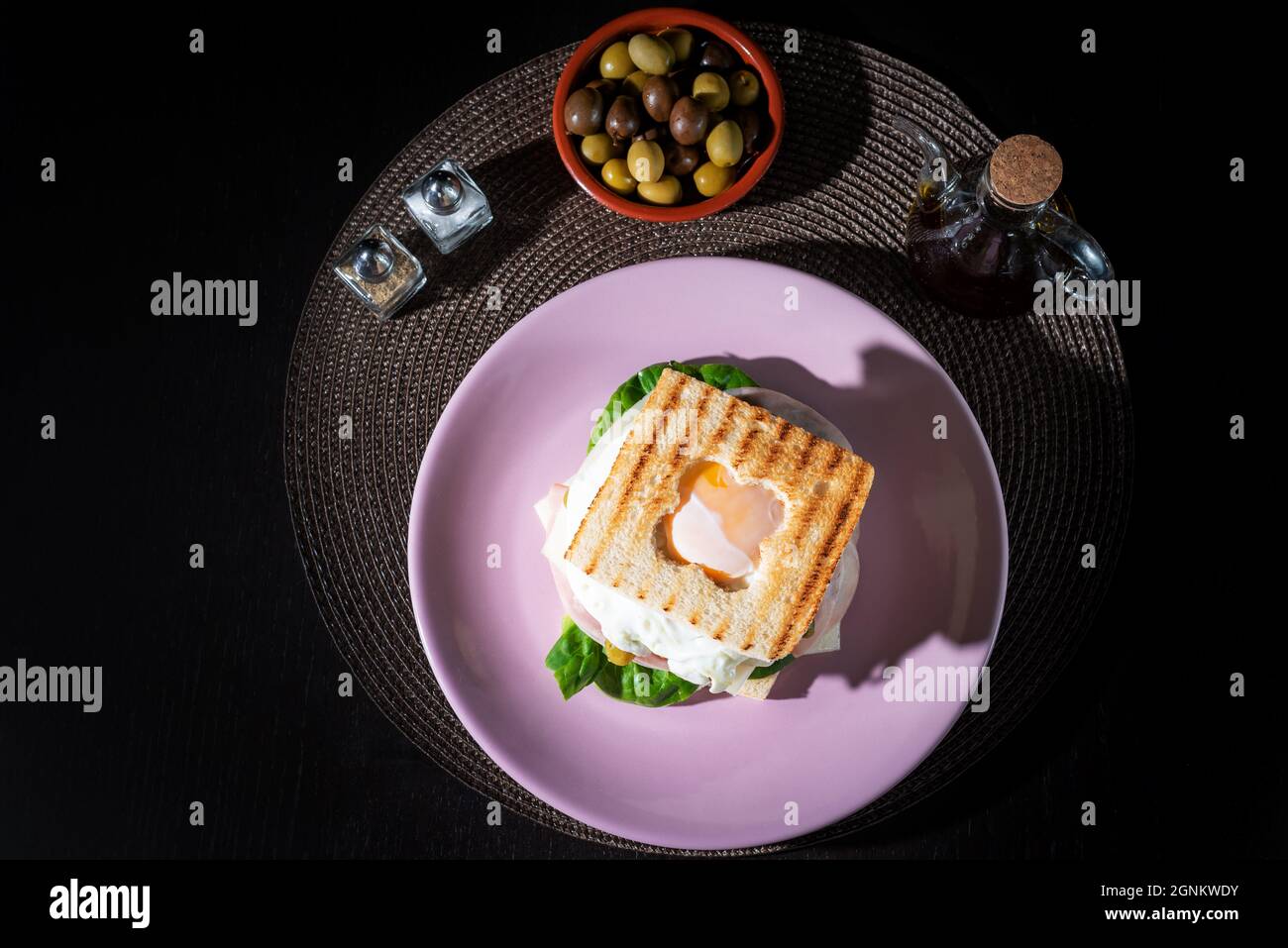 Sandwich aus Schinken, Käse, Salat, Gurken und einem Spiegelei, mit einer Öffnung in der oberen Pfanne, um das Eigelb des Eies zu zeigen, Draufsicht. Stockfoto