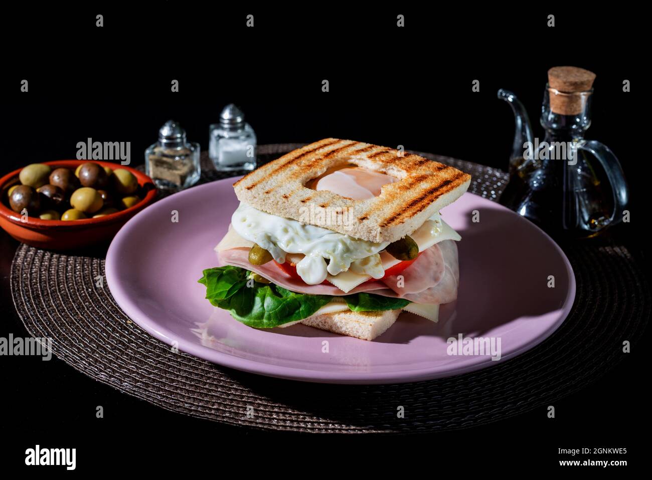 Sandwich aus Schinken, Käse, Salat, Gurken und einem Spiegelei, mit einer Öffnung im oberen Brot, so dass das Eigelb des Eies zu sehen ist. Stockfoto