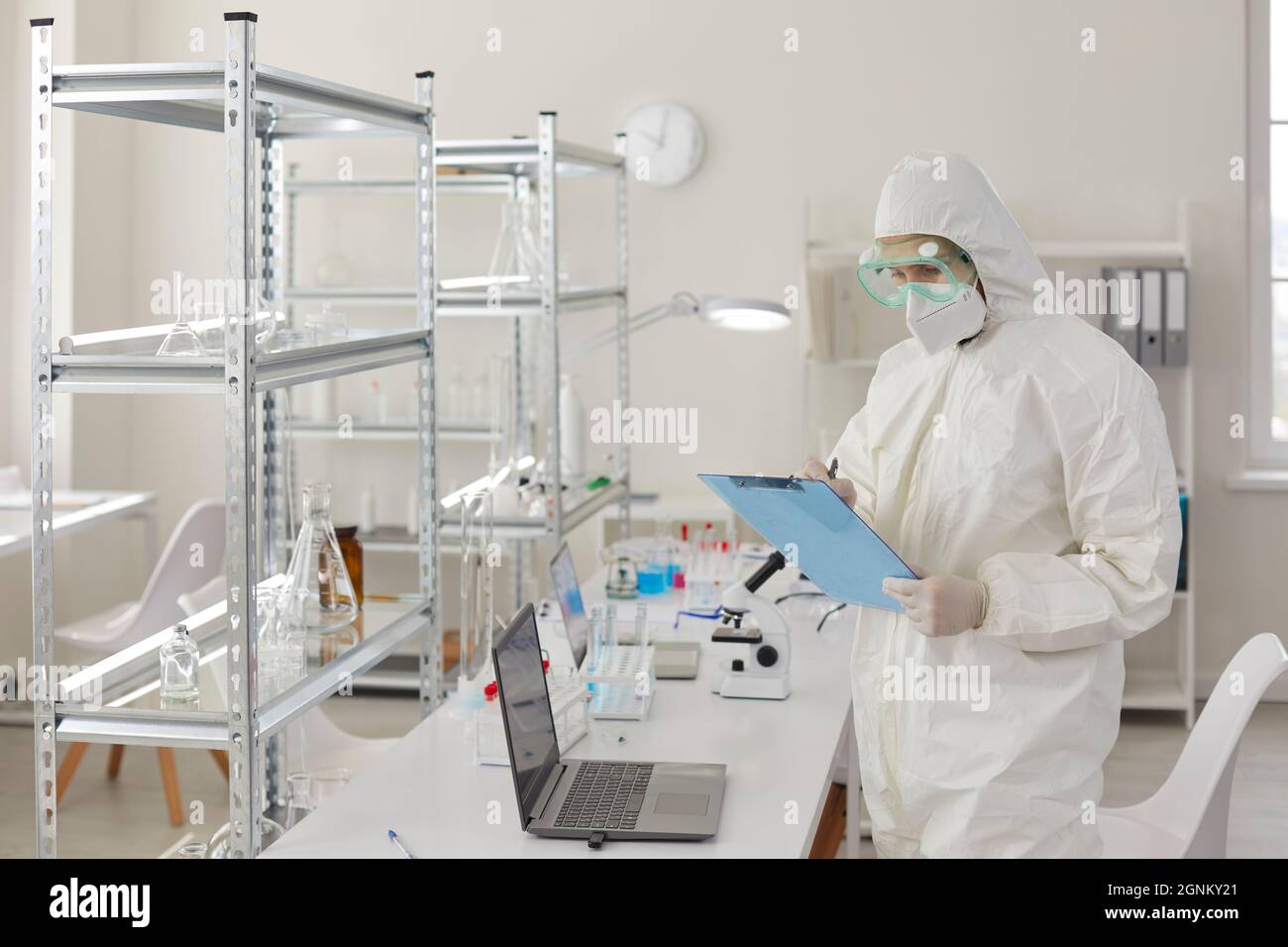 Wissenschaftler oder Arzt in einem schützenden medizinischen Anzug macht sich Notizen über das Experiment im Labor. Stockfoto